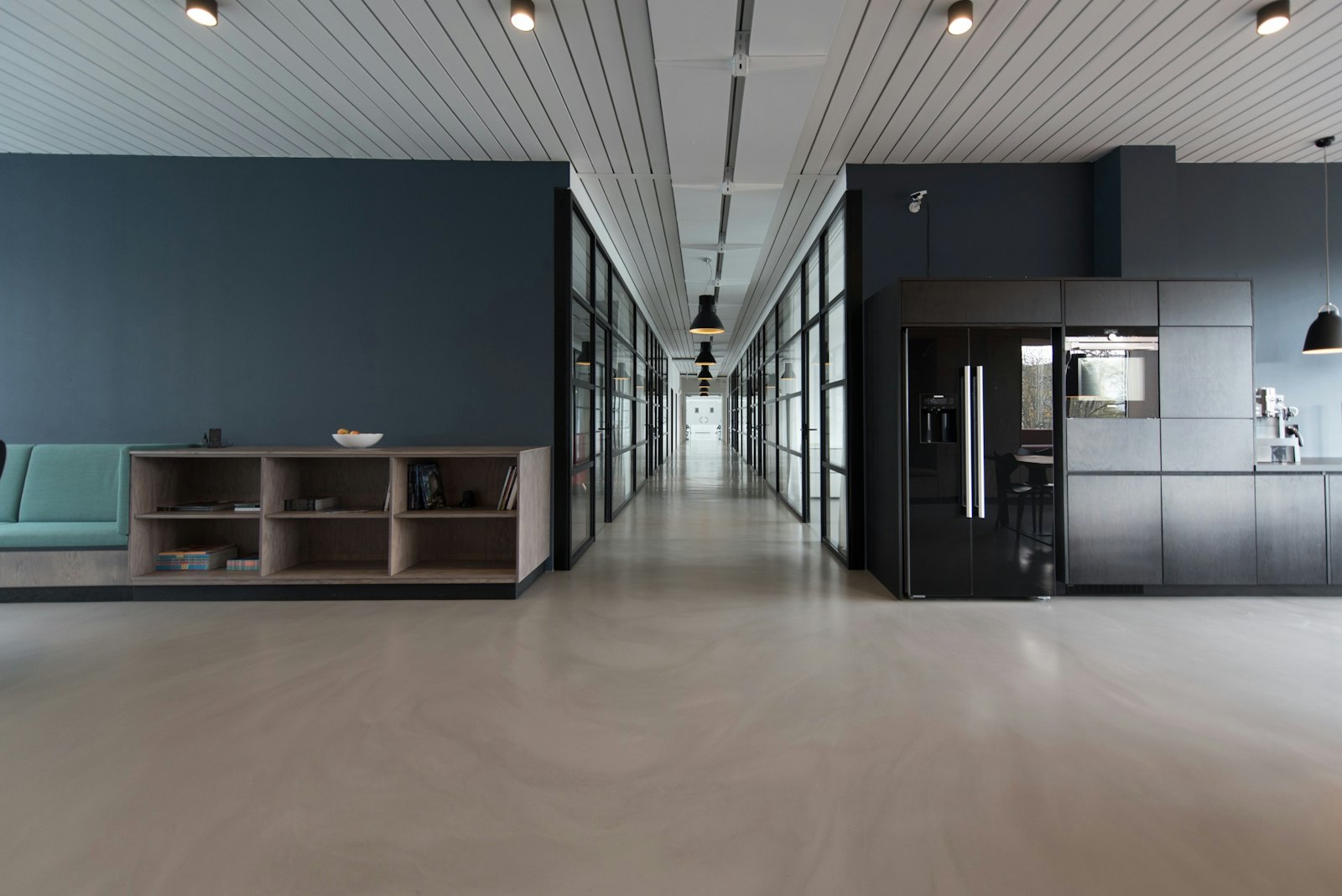 A modern office corridor with glass rooms and a shared kitchen.