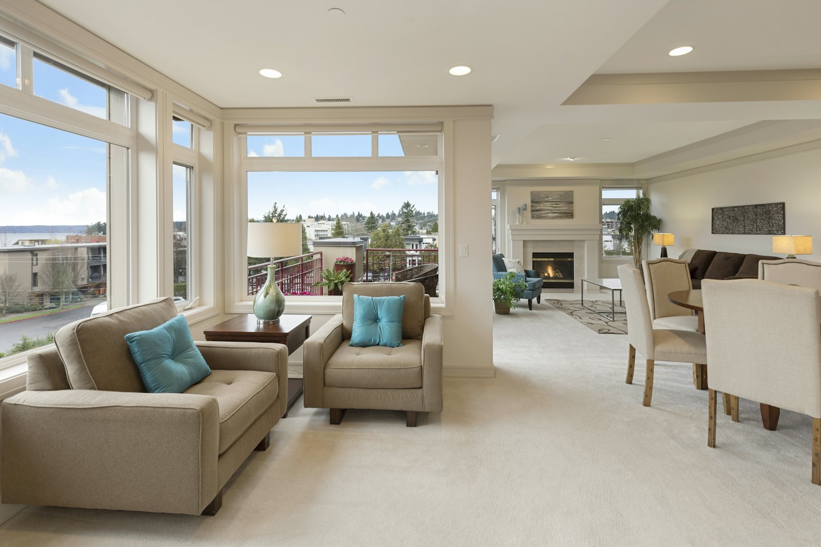 A bright staged living room with large windows and a fireplace.